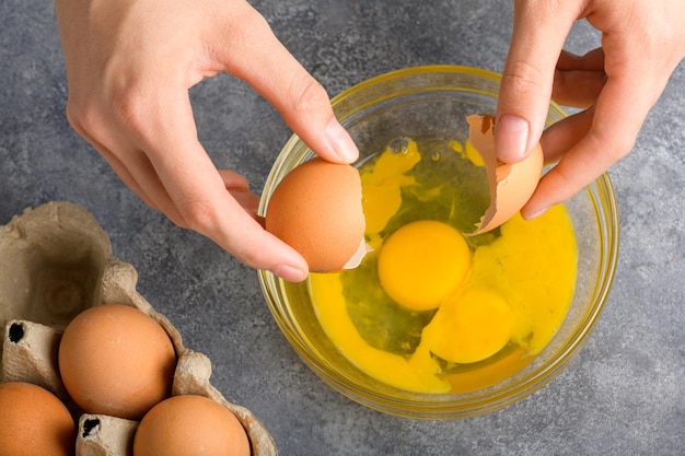 Housewife hands cracking fresh egg yolk and white dropping in a bowl top view