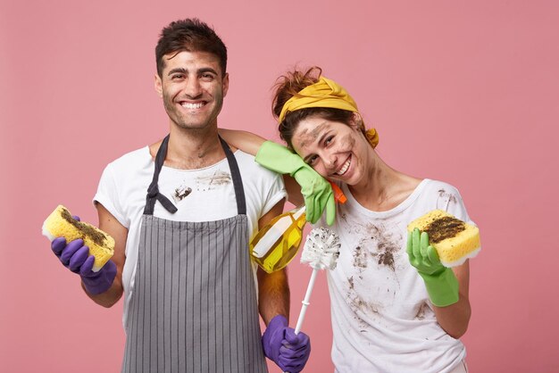 Housewife and her husband standing close to each other holding sponge brush and cleaning solution