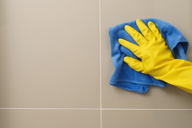 The housewife is using a cloth to clean the bathroom wall