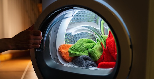 La casalinga apre una lavatrice o un'asciugatrice di notte con molti asciugamani colorati e puliti