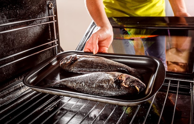 Домохозяйка готовит рыбу дорадо в духовке, вид изнутри духовки. Приготовление в духовке.