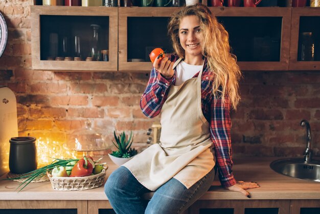 Housewife sits on table and holds tomato in hand