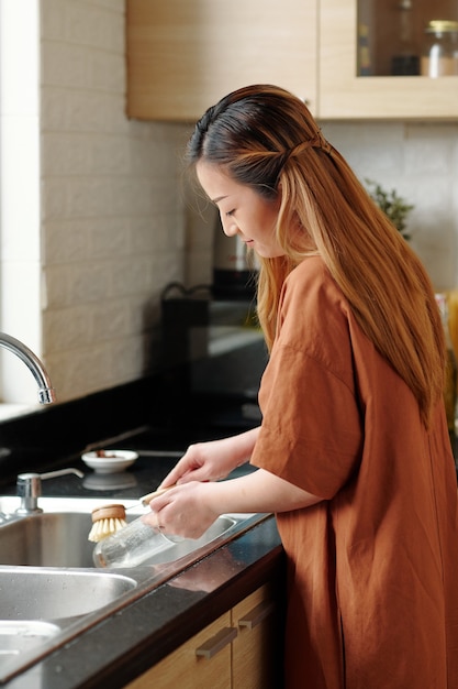 Housewife washing glass or vase with brush in kitchen sink