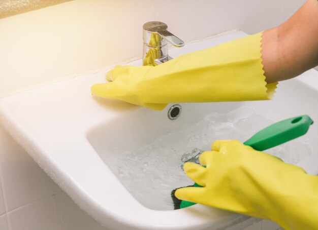 Housewife wearing yellow rubber glove and using brush cleaning basin in the toilet