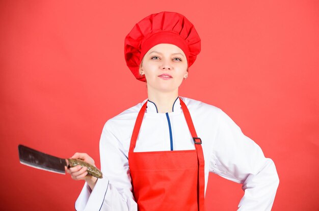 Casalinga con coltello da cucina macellaio taglia carne donna in cappello  da cuoco e grembiule chef professionista in cucina cucina donna felice che  cucina cibo sano secondo la ricetta aggiungendo un po 