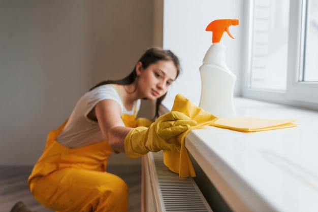 Housewife in yellow uniform works with window and surface cleaner indoors House renovation conception