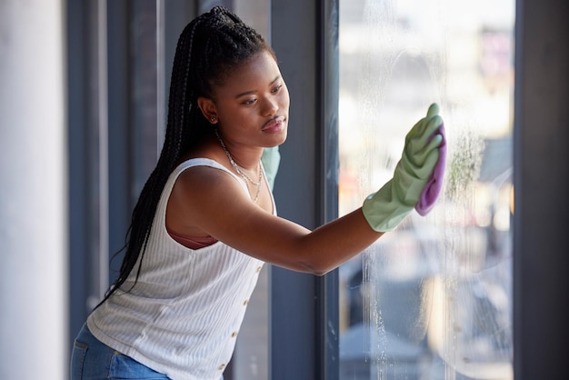 Гигиена по дому и чернокожая женщина моет окно тканью, занимаясь уборкой в доме. Уборка и африканская уборщица или домохозяйка, моющая стеклянную дверь от пыли или грязи.
