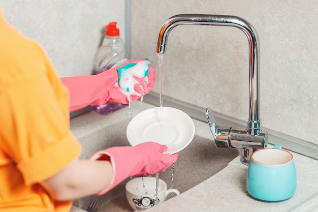 Housework. A woman in pink rubber gloves is washing dishes. View from the shoulders