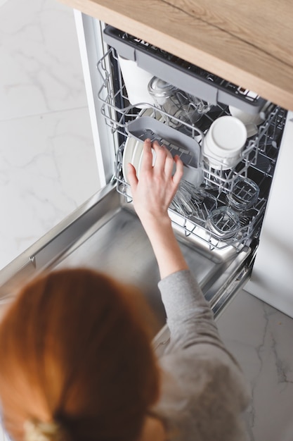 Housework: young woman putting dishes in the dishwasher