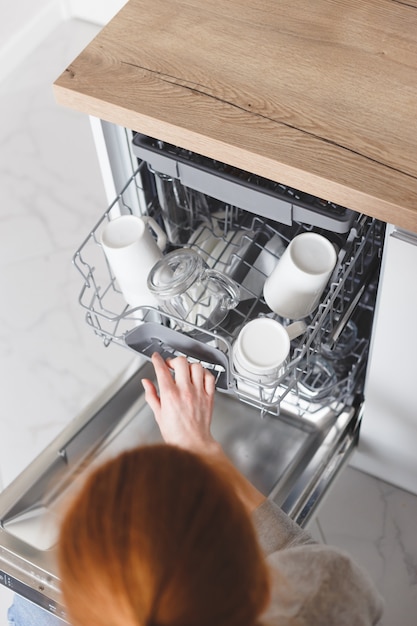 Housework: young woman putting dishes in the dishwasher