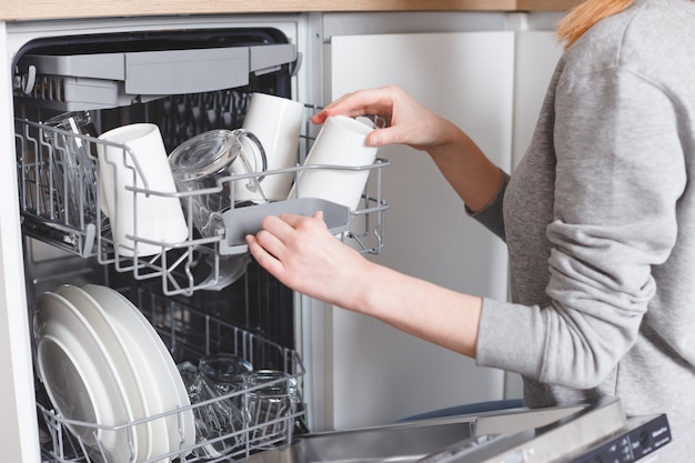 Lavori domestici: giovane donna che mette i piatti in lavastoviglie