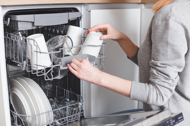 Housework: young woman putting dishes in the dishwasher