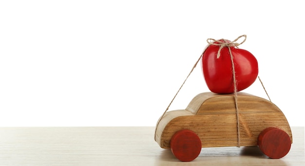 Houten auto met een rood hart eraan vastgebonden op een witte houten tafel