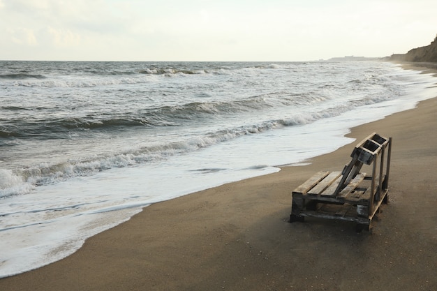 Houten bankje op zandstrand aan zee, ruimte voor tekst