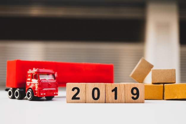 Houten blokjaar 2019 met vrachtwagenvoertuig en kartondozen die als logistiekconcept gebruiken