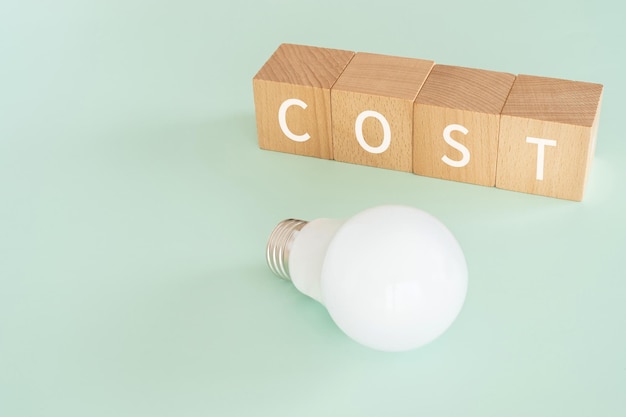 Houten blokken met COST-tekst van concept en een gloeilamp.