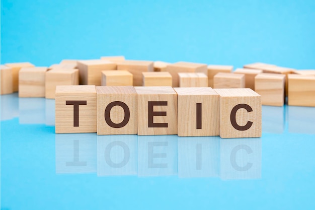 Houten blokken met de letters TOEIC op het heldere oppervlak van een blauwe tafel, de inscriptie op de kubussen wordt gereflecteerd door het oppervlak TOEIC Test of English for International Communication