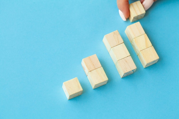 Houten blokken met een menselijke hand die een kubus bovenaan op een blauwe achtergrond plaatst