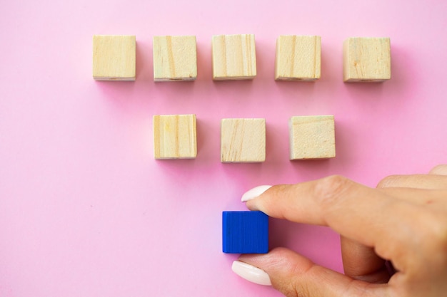 Houten blokken met een menselijke hand die een kubus bovenaan op een roze achtergrond plaatst