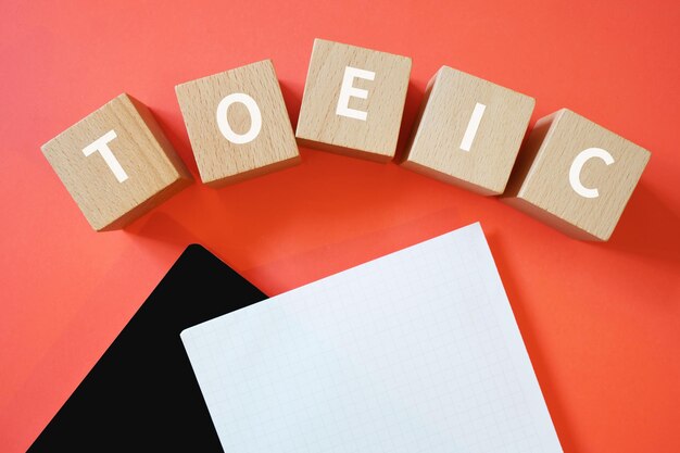 Houten blokken met TOEIC-tekst van concept, papier en een notitieboekje.