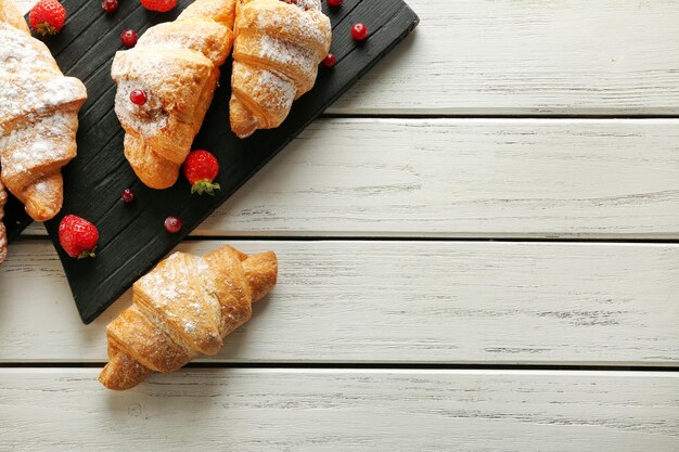 Houten bord met lekkere croissants en bessen op tafel