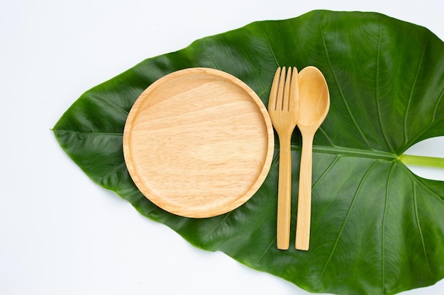 Houten bord met lepel en vork op groene bladeren