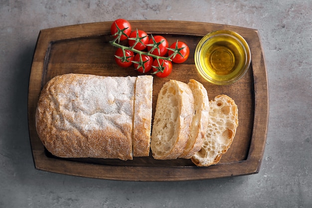 Houten bord met olijfolie, vers brood en tomaten op tafel