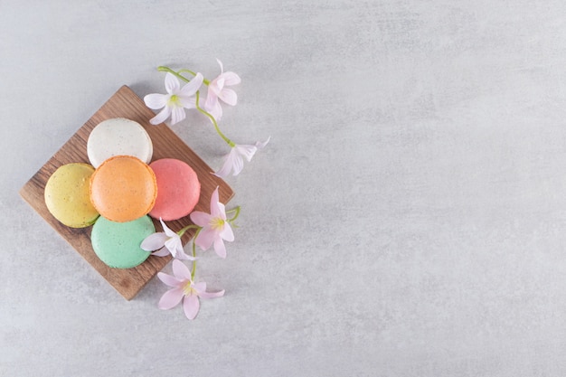 Houten bord van kleurrijke zoete bitterkoekjes met bloemen op stenen tafel.