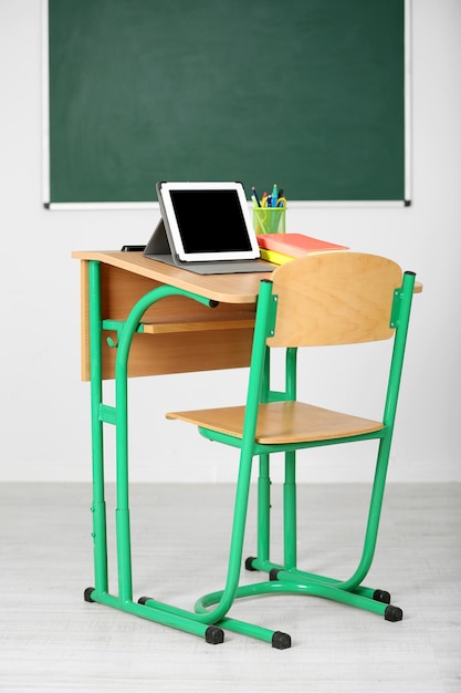 Houten bureau met briefpapier en tablet in de klas op schoolbordachtergrond