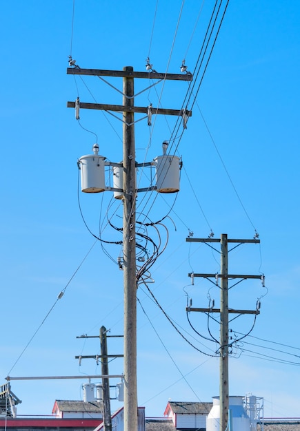 Houten elektriciteitspaal met gemonteerde transformatoren op blauwe hemelachtergrond