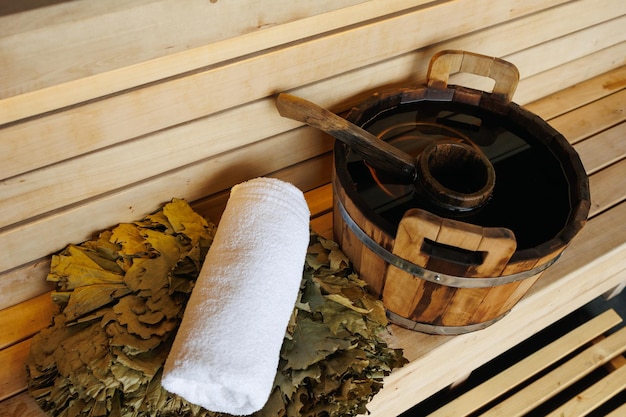 Houten emmer met pollepelhanddoek en bezem op bank in sauna