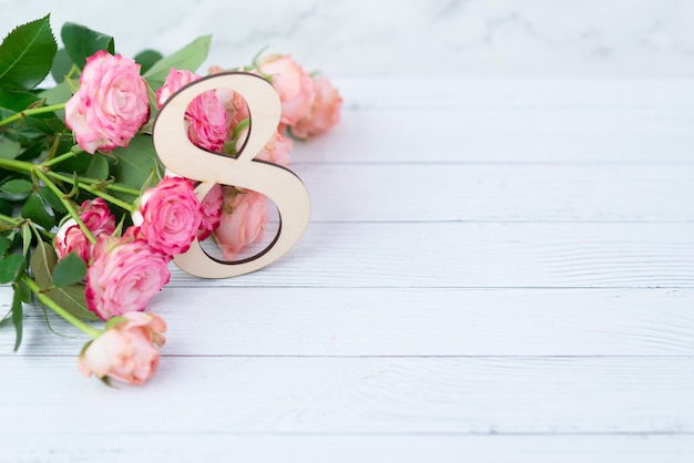 Houten figuur 8 met roze bloemen op een witte tafel. Internationale vrouwendag. 8 Maart