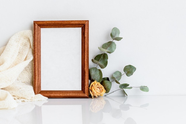 Houten fotolijst met een takje eucalyptus en een gele roos op een witte houten tafel minimalistische delicate lay-out blanco voor een ansichtkaart