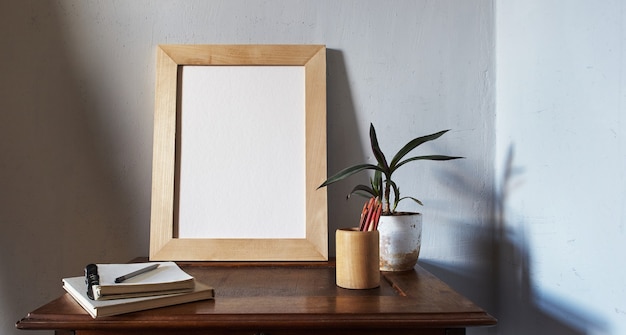 Houten fotolijst mockup. bloempot op een stapel boeken op een oud houten bureau. samenstelling op een witte muur