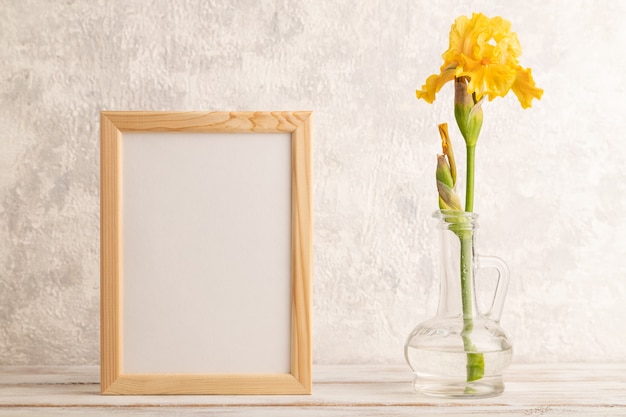 Houten frame met gele irisbloem in glas op grijze betonnen ondergrond. zijaanzicht, kopieer ruimte