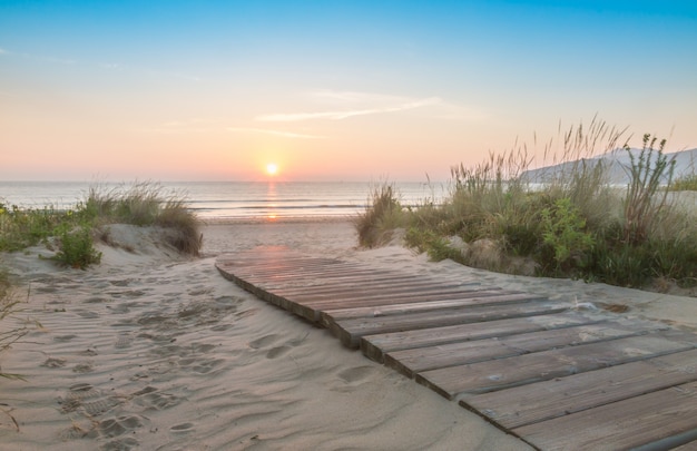 Houten gang die het strand ingaat bij zonsopgang