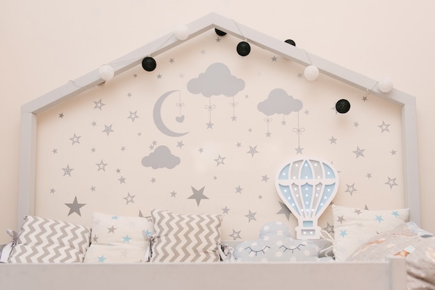 Houten grijs wit babybed in de vorm van een huis met sterren en maan aan de muur, houten nachtlampje in de vorm van een ballon, kinderkamer inrichting