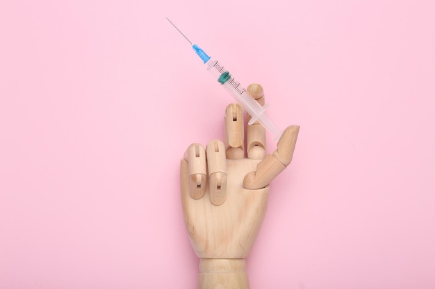 Houten hand houdt injectiespuit vast op roze achtergrond Vaccinatie