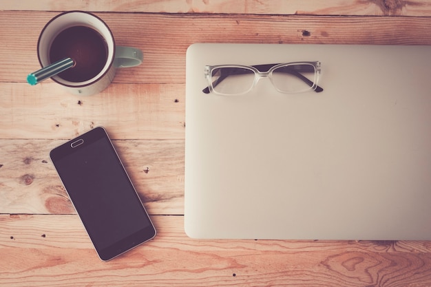 Houten hipster moderne bureautafel met laptop, koffie, smartphone en bril - vlakke laagfoto voor modern technologiewerkconcept - werkstation thuis met veel apparaten