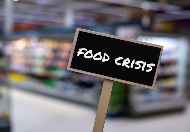 Houten informatielabel met tekst FOOD CRISIS tegen onscherp bericht in winkelschappen