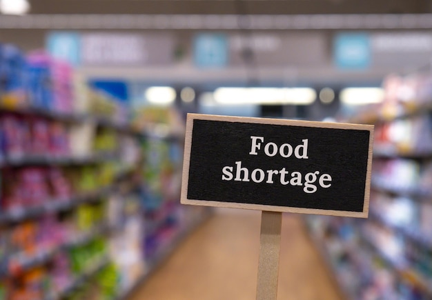 Houten informatielabel met tekst FOOD SHORTAGE tegen onscherp bericht in winkelschappen