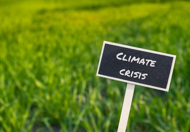 Foto houten informatielabel met tekst klimaatcrisis tegen onscherp landbouwveldbericht