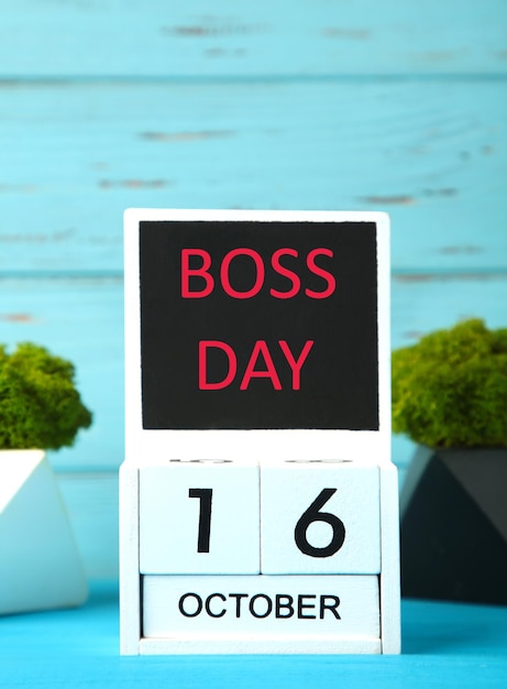 Foto houten kalender met inscriptie boss day met groene planten boss day concept op blauwe achtergrond