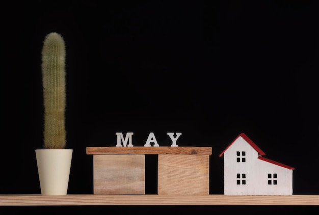 Houten kalender van mei cactus en huis model op zwarte achtergrond kopie ruimte