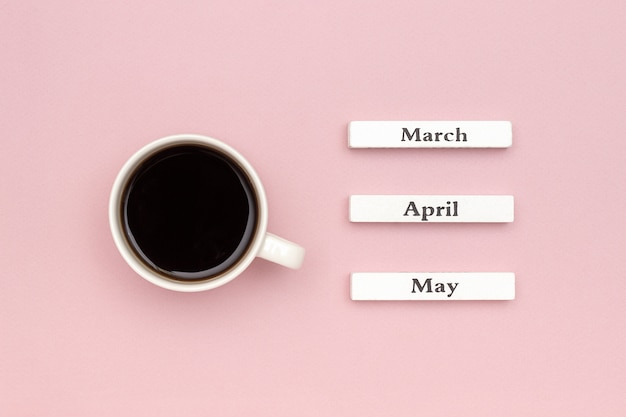 Houten kalender voorjaar maanden maart april mei en kopje zwarte koffie gericht op mei op pastel roze papier achtergrond.