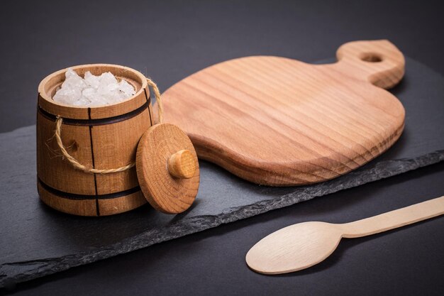 Houten klein vat voor het bewaren van zoutlepel en snijplank met stenen bord op zwarte achtergrond