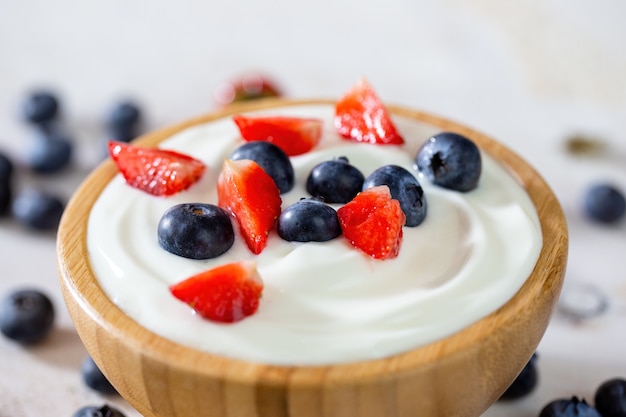 Houten kom gevuld met yoghurt, aardbeien en bosbessen in detail