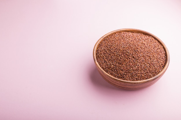 Houten kom met rauwe rode quinoa zaden op een pastel roze achtergrond. Zijaanzicht, kopieer ruimte.