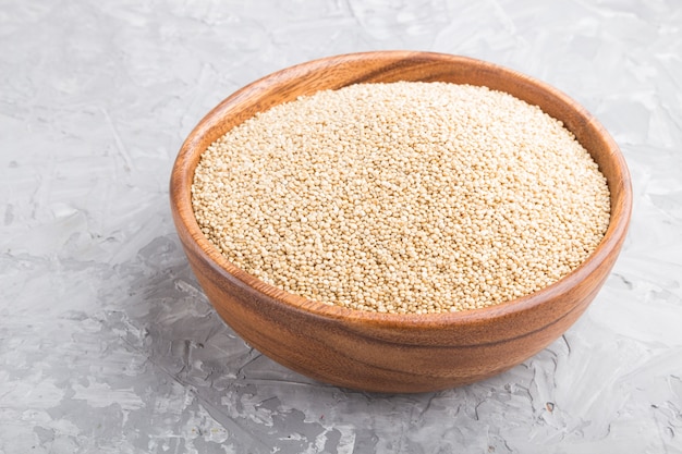 Houten kom met rauwe witte quinoa zaden op een grijze betonnen tafel. zijaanzicht, close-up.