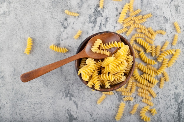 Houten kom rauwe fusilli pasta op stenen oppervlak.